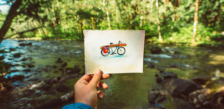 A person holds up a sketch of a bicycle in nature