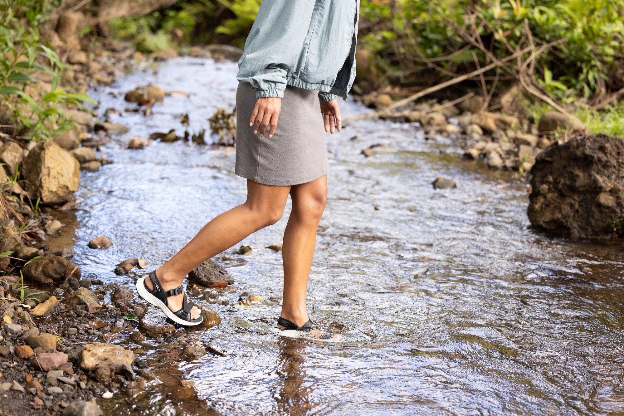 a woman crossing a stream in sandals