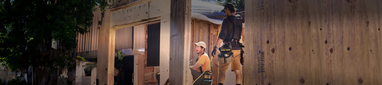 Two men wearing construction gear using hammers to work on building a house frame. 