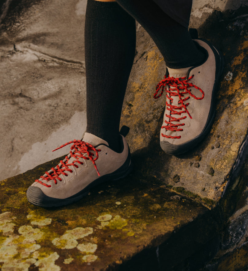 Knee-down shot of woman wearing suede tan and orange Jasper sneakers  with knee high black socks while standing on cement block
