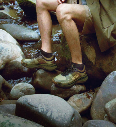 Knee-down shot of man wearing green Versacore waterproof shoes and sitting on rocks over river