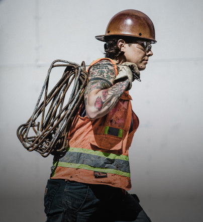 A woman in construction vest and helmet carrying metal coils across building site