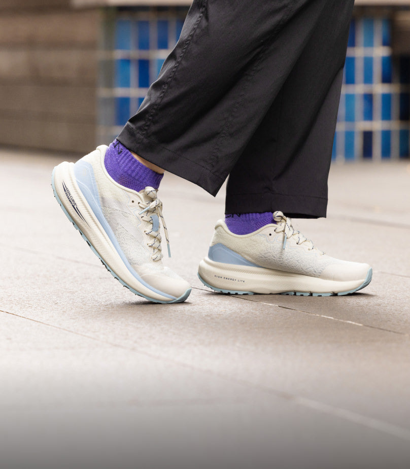 Knee-down shot of woman wearing white and light blue WK500 walking shoes with purple socks and black 