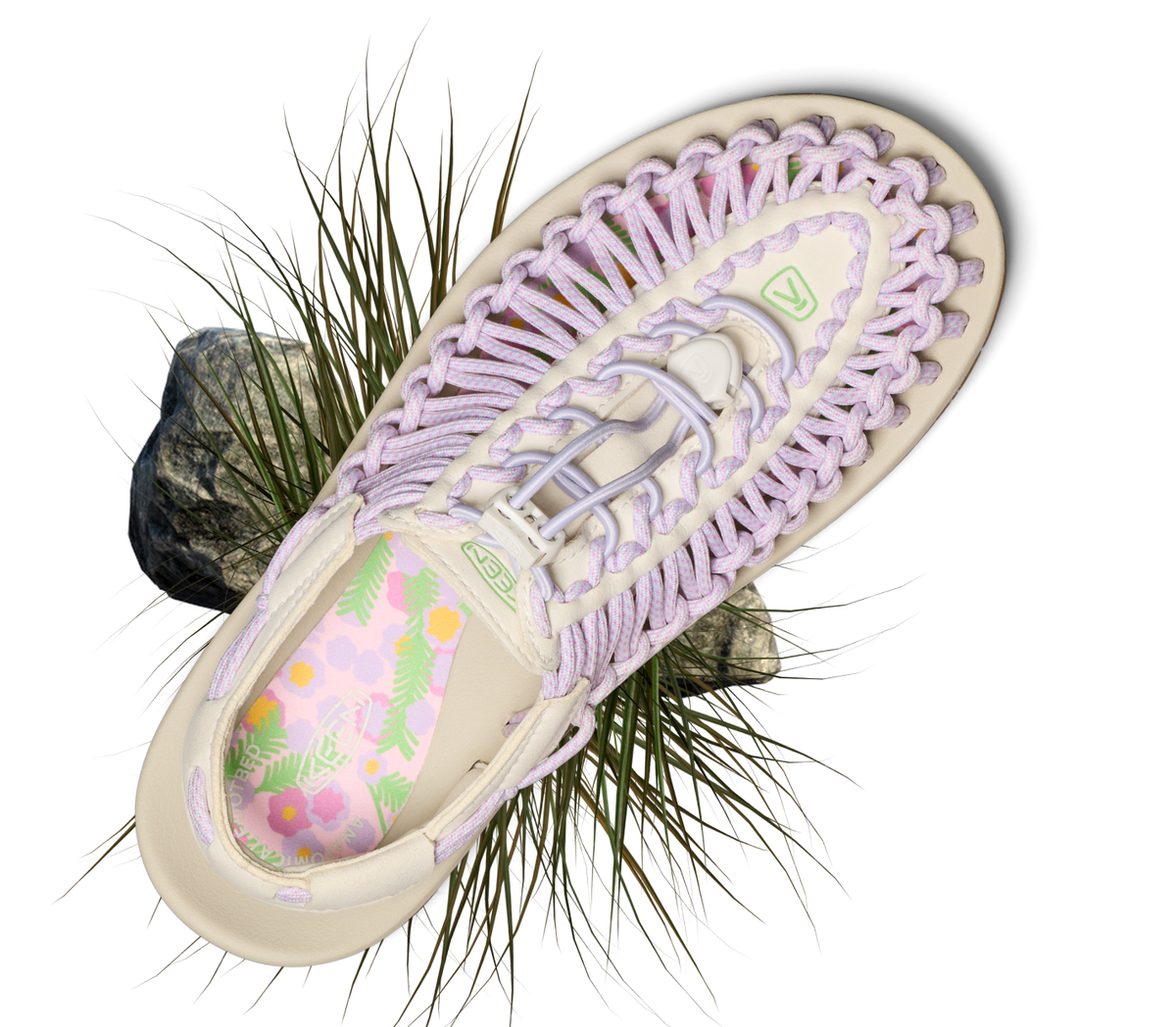 Product shot of lavender and cream uneek open-air sandal with grassy detail surrounding the product. 
