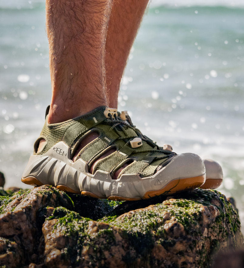 Person wearing green KEEN sandals on a rock by the water