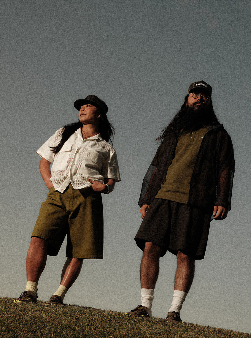 Two people standing on a hilltop in stylish baggy shorts, overlooking a scenic landscape under a clear blue sky.