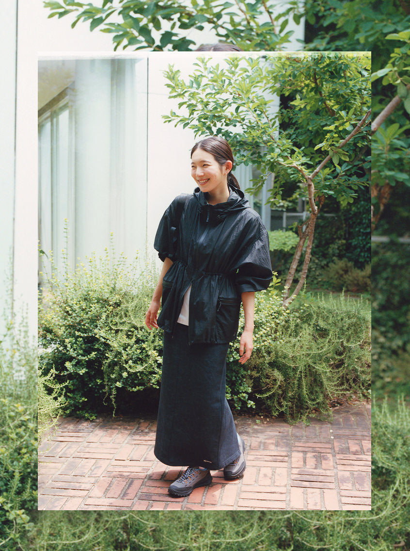 Knee-down shot of woman in long green skirt wearing KEEN and Skall collaboration Jasper sneakers with brown leather and white and green laces on crunchy fall leaves. 