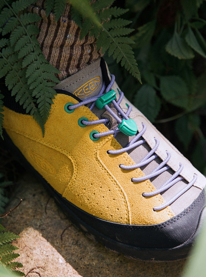 Close-up of a split color shoe, half yellow and half purple, featuring vibrant green bungee-laces, showcasing its unique color combination and design details.