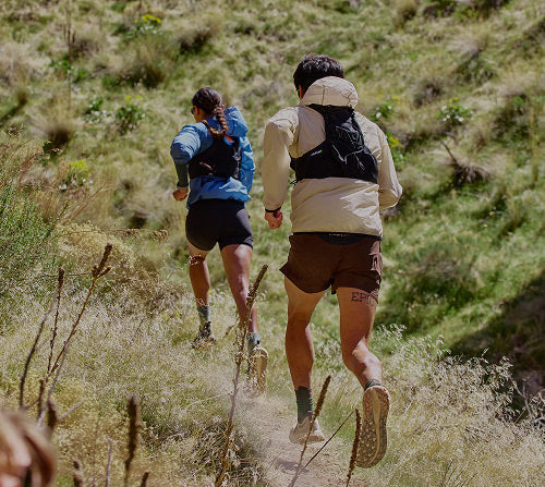 Two people running on a high-desert trail, showcasing Roam trail running shoes in a natural outdoor setting.