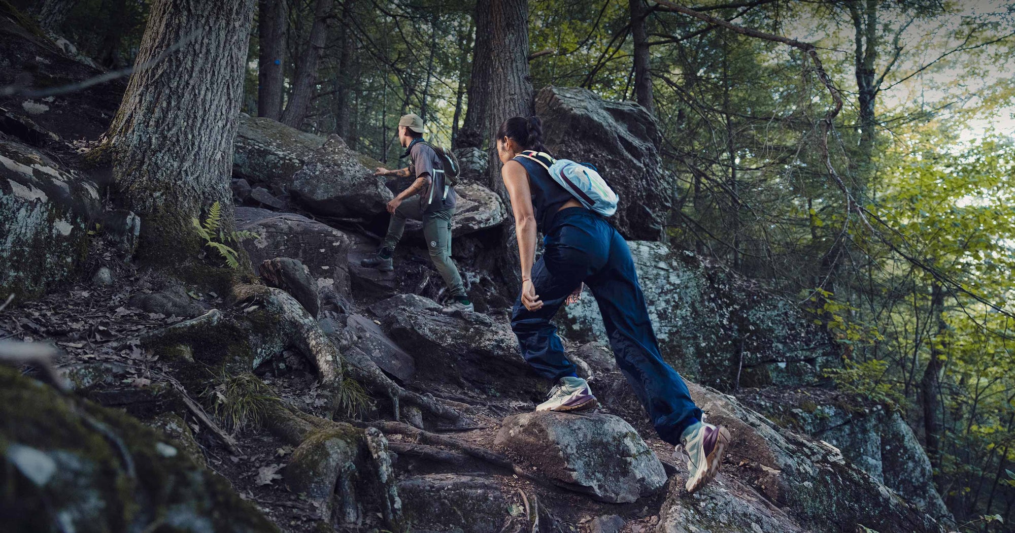  A man and a woman hike up a rocky trail in the woods, wearing Targhee Apex shoes for support and traction.