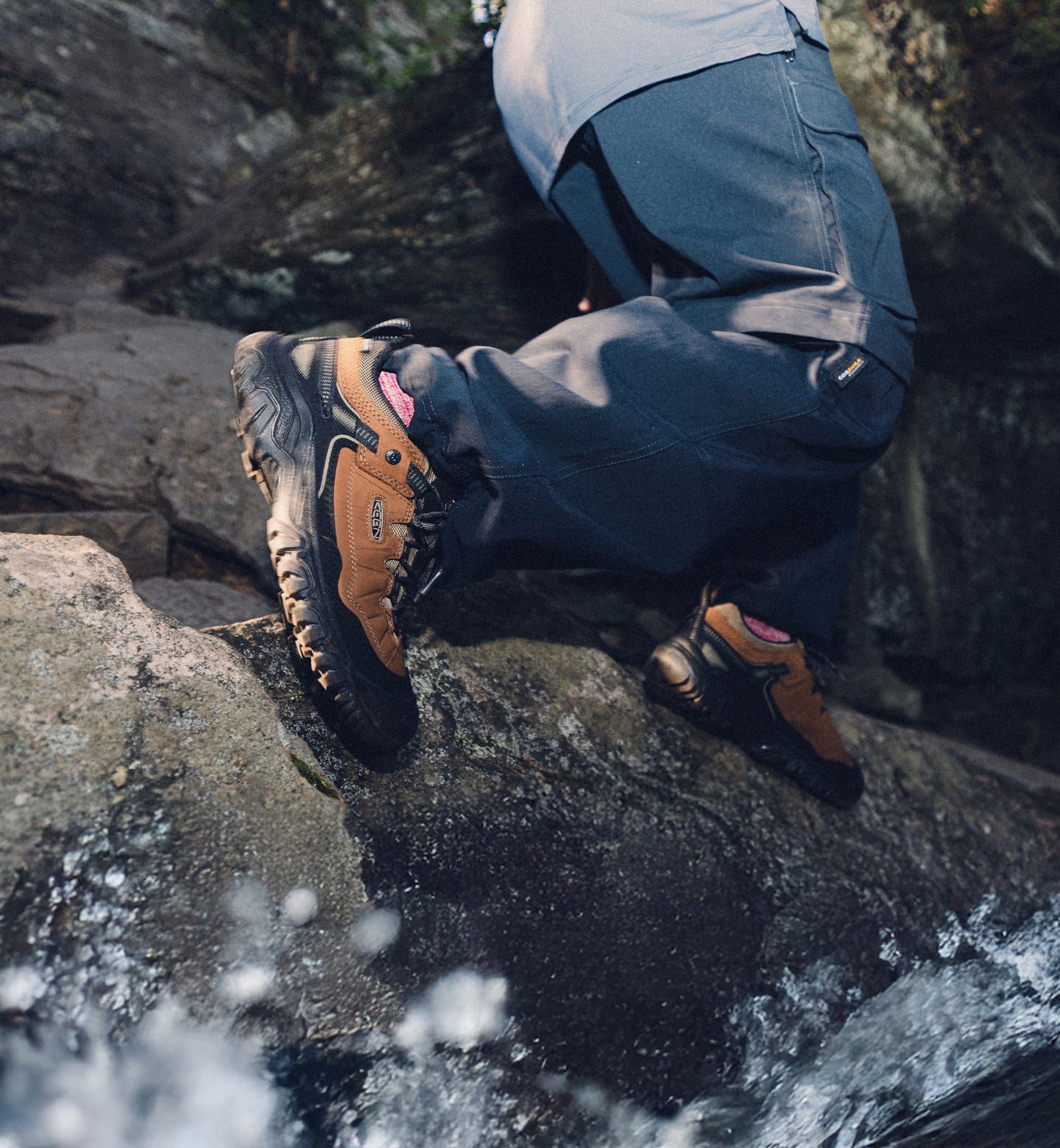 Man wearing waterproof Targhee IV hiking shoes and stepping across river rocks while water splashes his feet. 