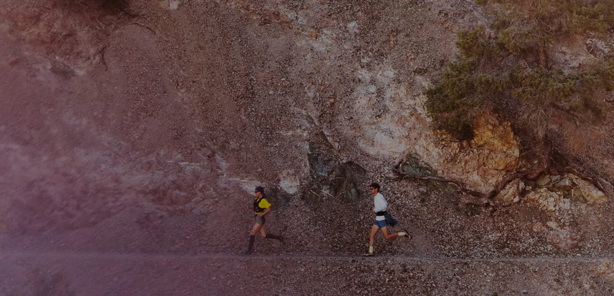 Two trail runners in mid stride alongside an impressive desert cliff. 