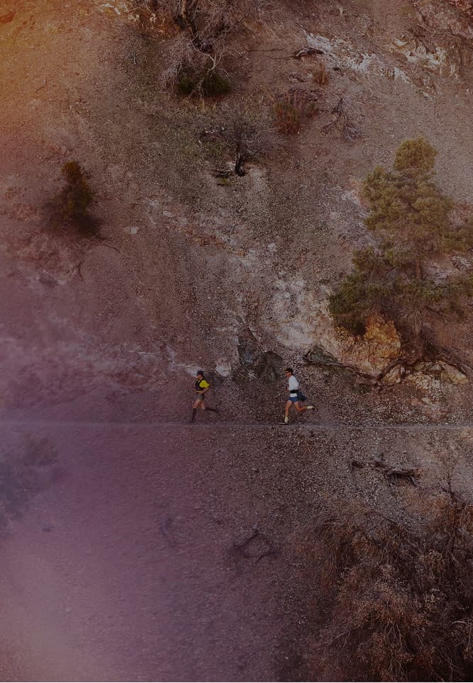 Two trail runners in mid stride alongside an impressive desert cliff. 