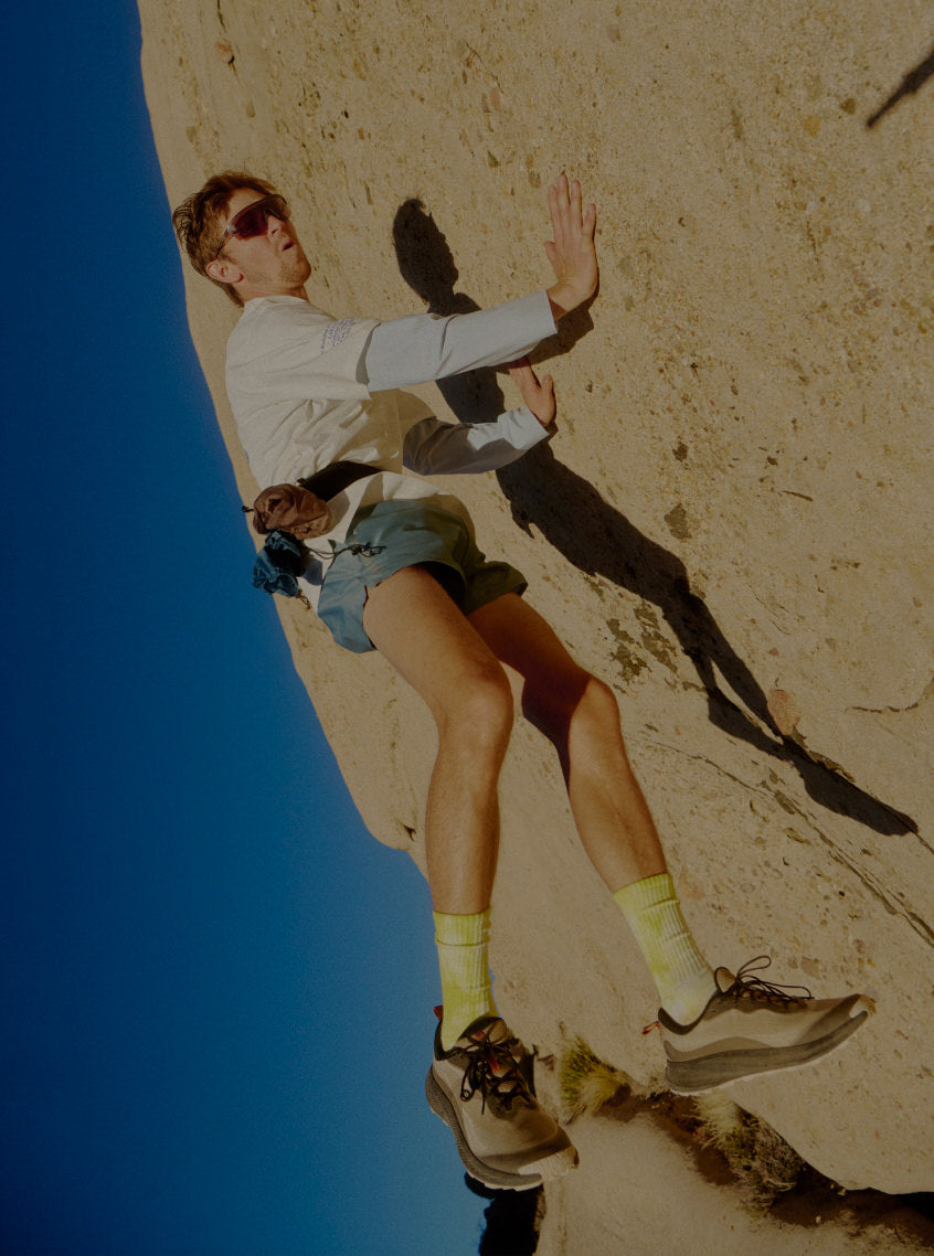 A  man with a running belt and bright yellow socks paired with Wander trail running shoes jumping up onto a rocky wall