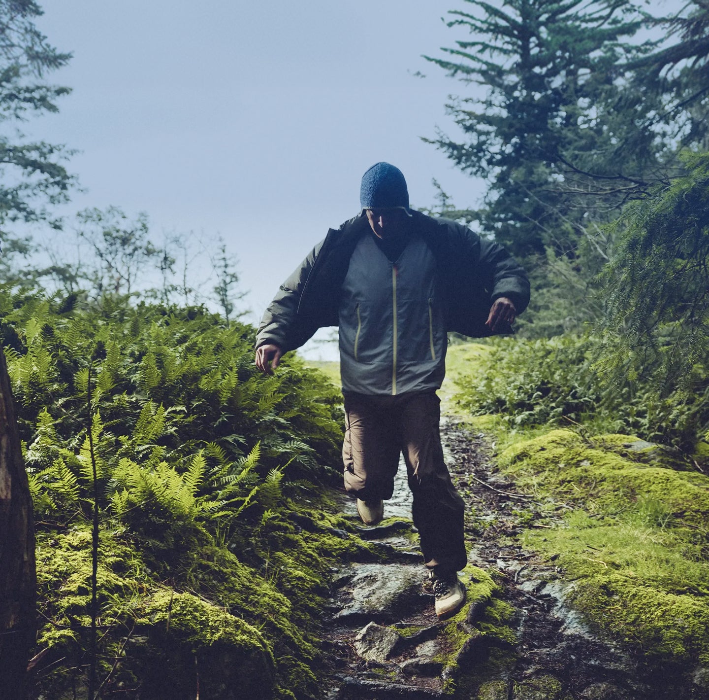 A man walking through muddy and wet terrain in a lush forest setting while wearing olive green hightrail hiking boots. 