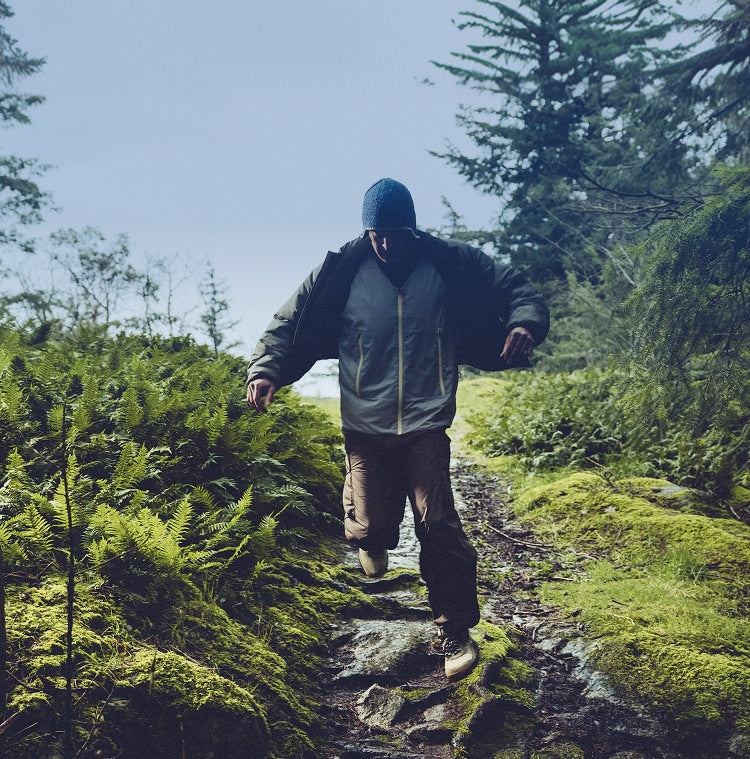 A man walking through muddy and wet terrain in a lush forest setting while wearing olive green hightrail hiking boots. 