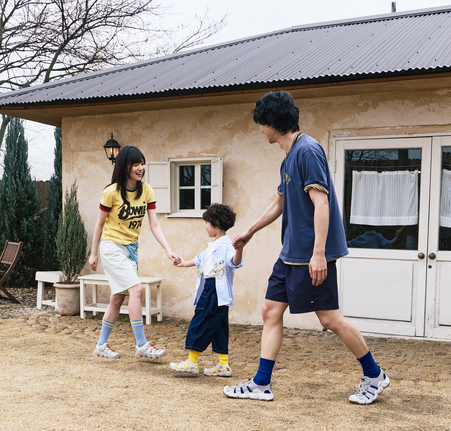 A mom, dad and daughter all wearing hyperport sandals and socks and holding hands while walking out of their house. 