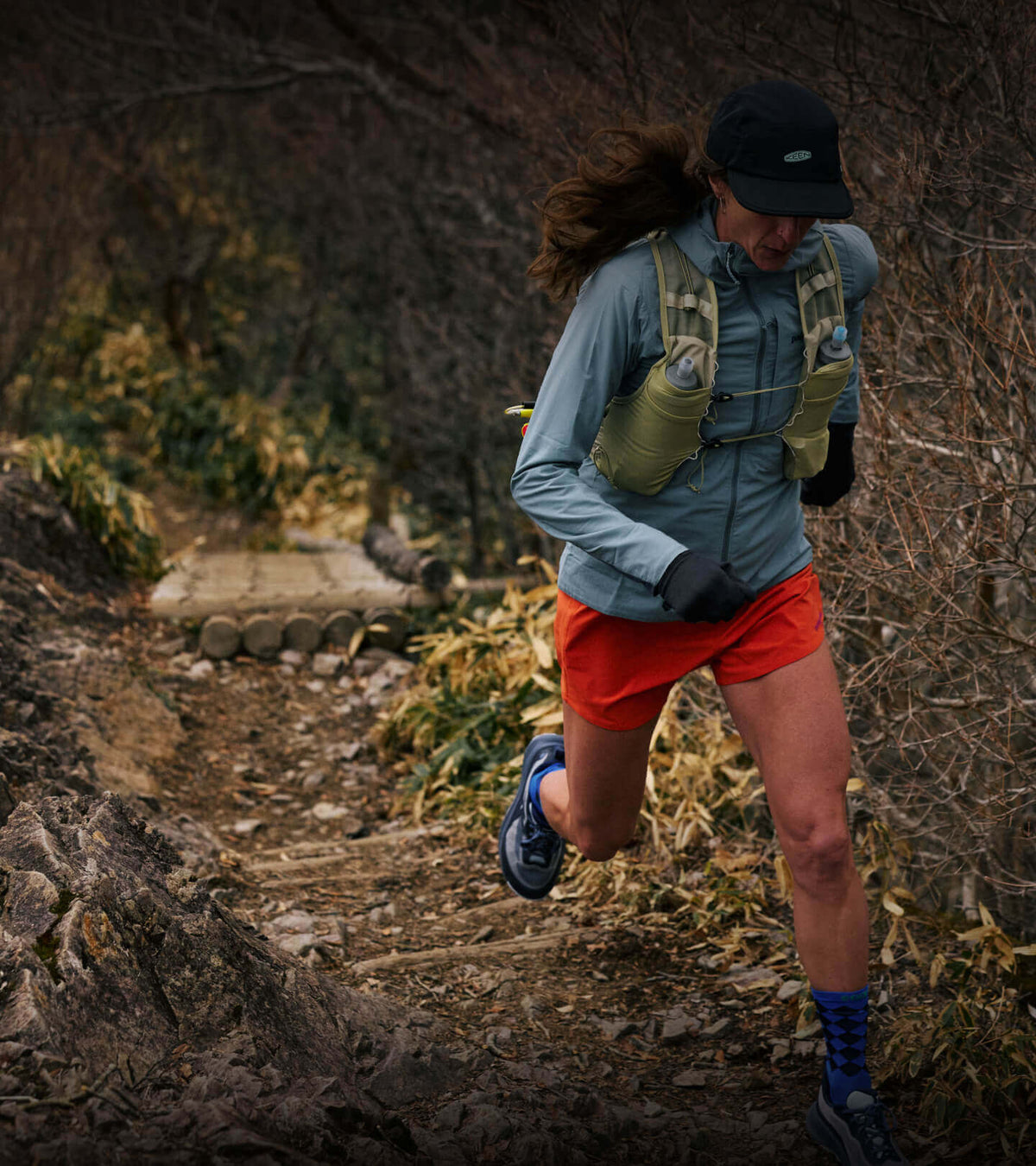 Woman running up mountain trail in fall with New KEEN Wander running shoes
