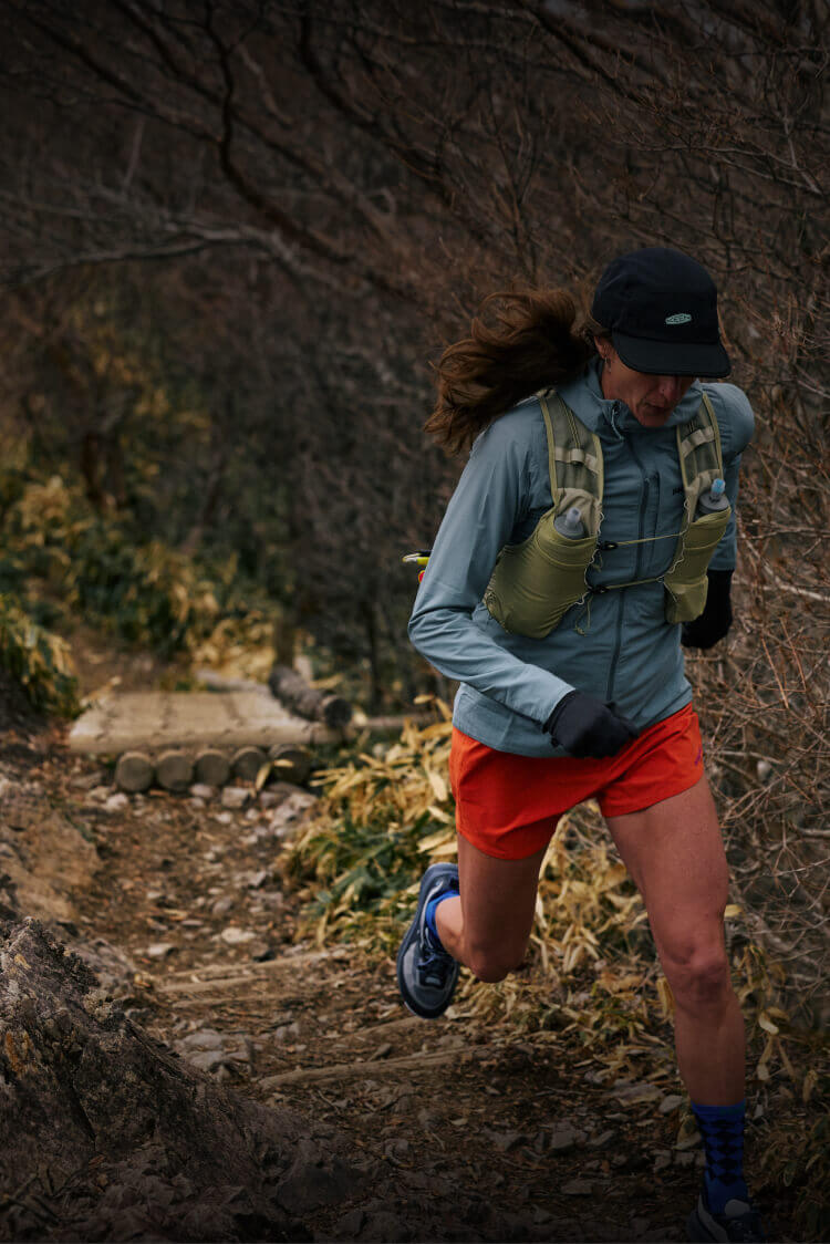 Woman running up mountain trail in fall with New KEEN Wander running shoes