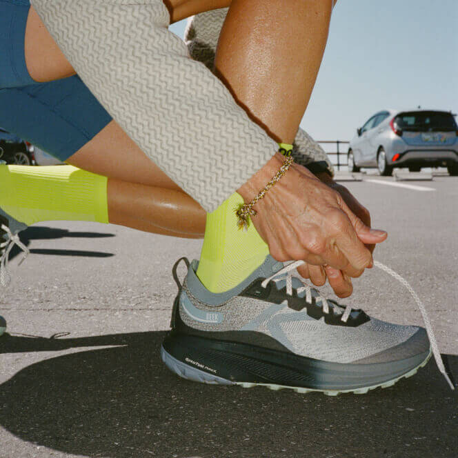 Person kneeling in parking lot tying shoe lace on Seek running shoe