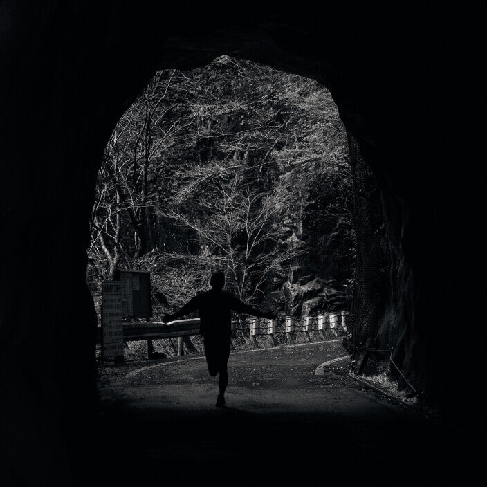 Runner silhouetted against tunnel opening on paved forested trail 