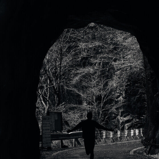 Runner silhouetted against tunnel opening on paved forested trail 