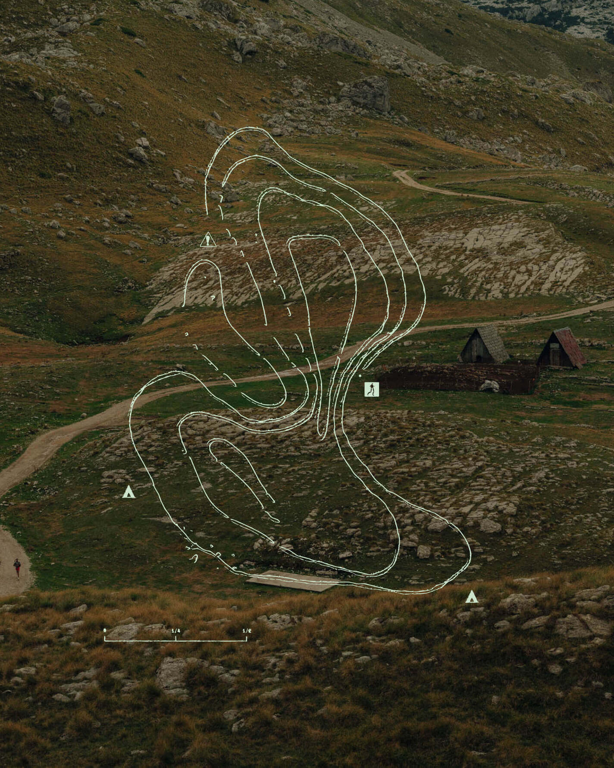 Topographic lines of hill overlayed onto a photo of a high mountain dirt road running past two A-frame houses 