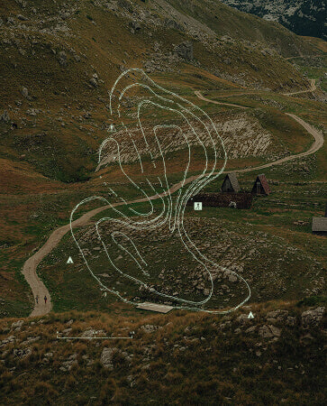 Topographic lines of hill overlayed onto a photo of a high mountain dirt road running past two A-frame houses 