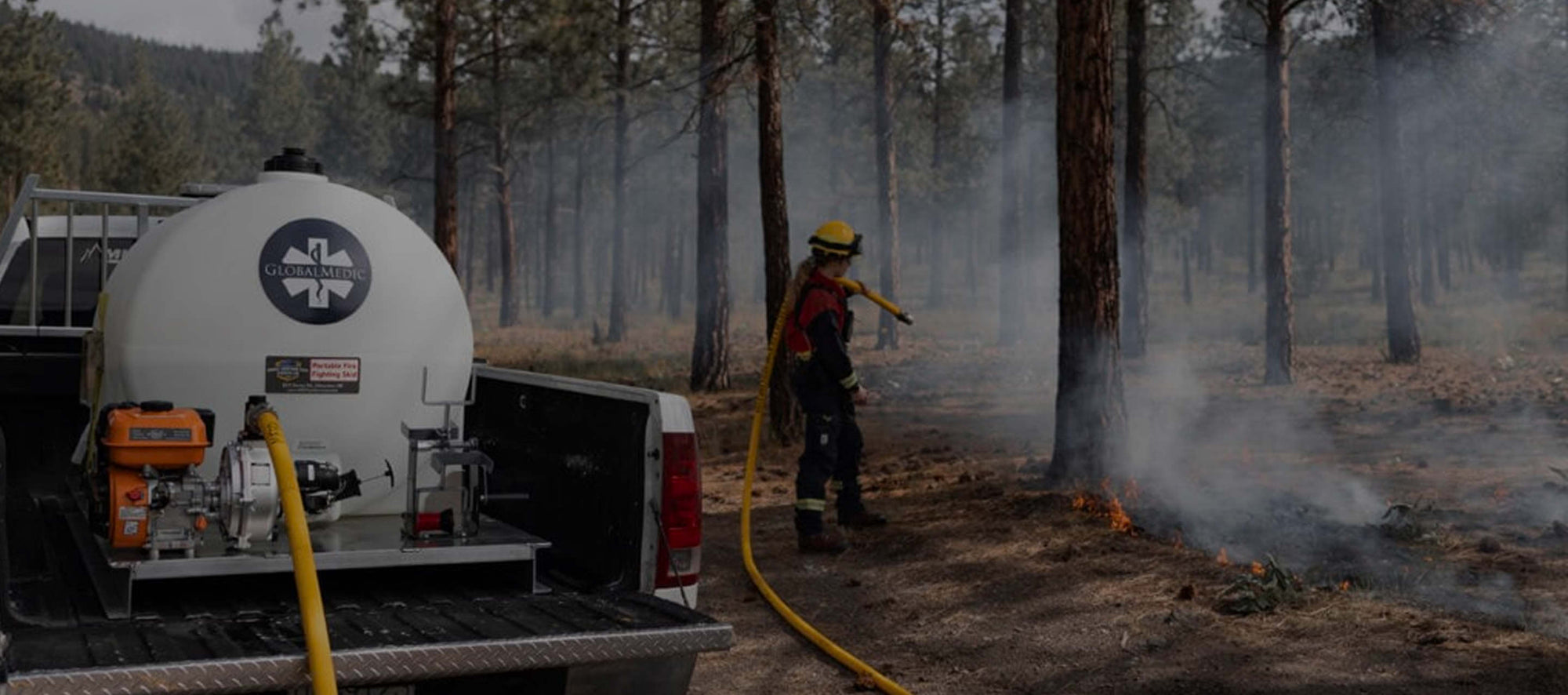 GlobalMedic Firefighter aiming hose at road side fire. 