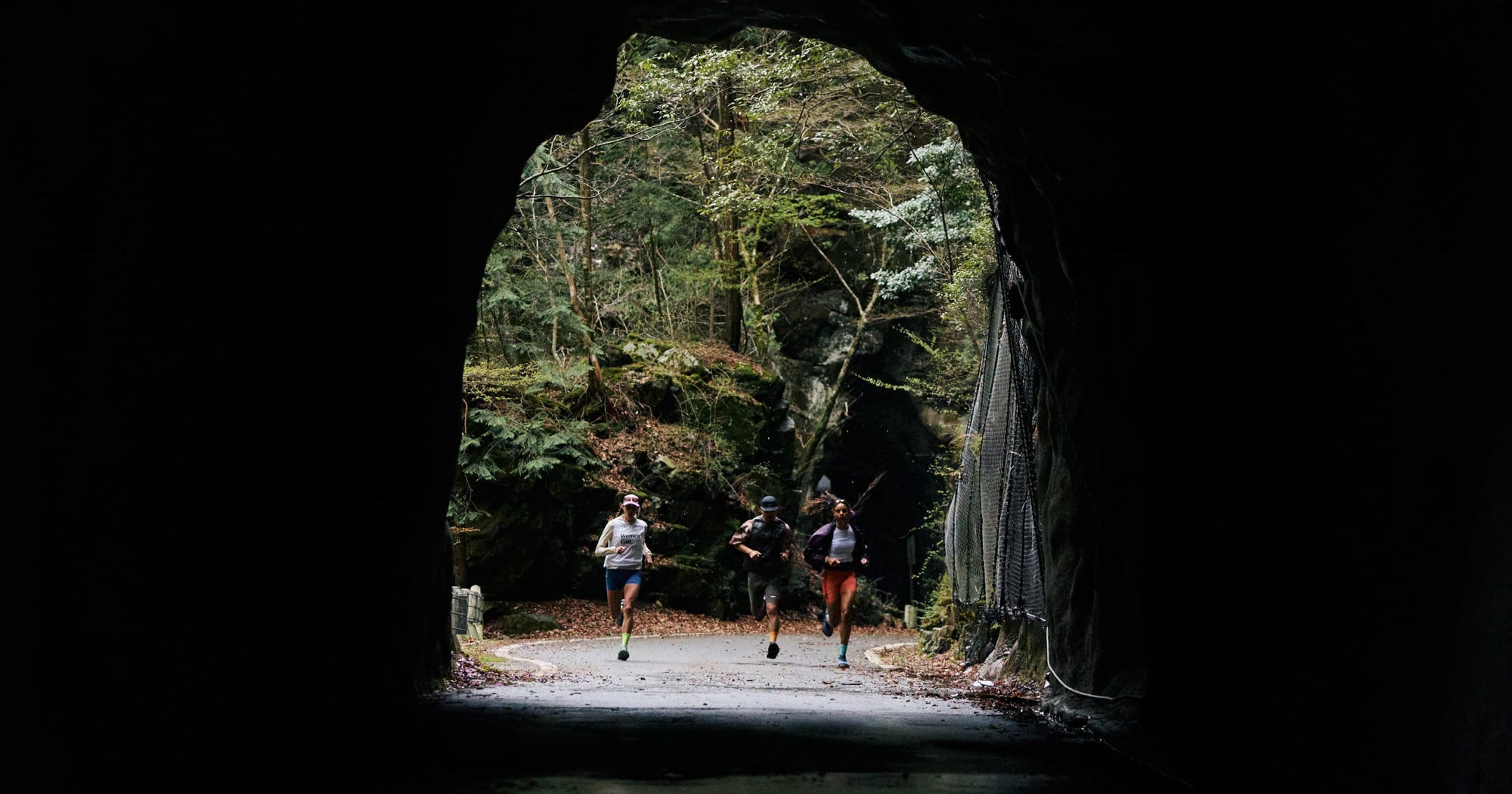 3 trail runners approaching a rocky runnel on a forested road. 