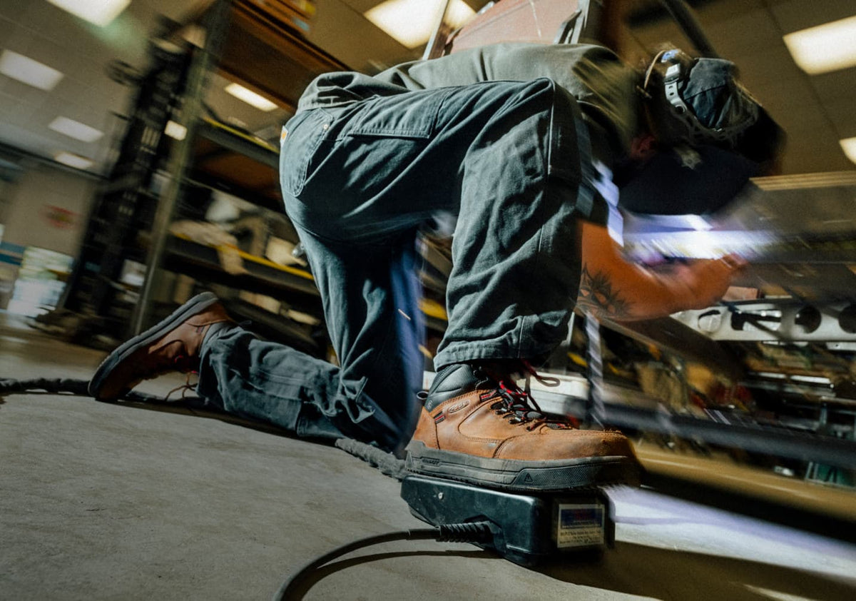 A man wearing Gibson Hiker Utility boots while operating welding machinery in a workshop setting. 