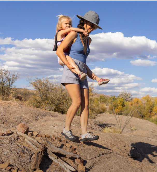 Woman with young child on back walking through desert landscape in Newport sandals