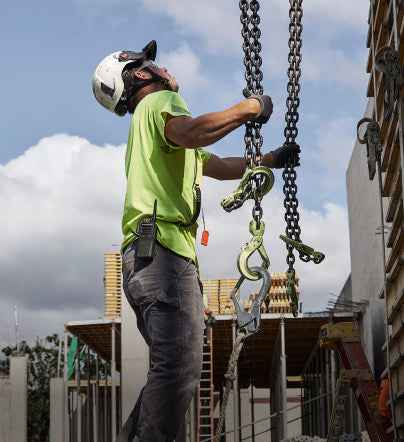 Man in construction clothing and helmet holding chain form large pulley system at construction site. 