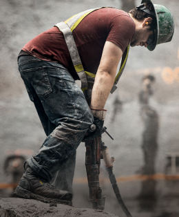 A man working outside on a job site, using a large tool to drill into the ground.