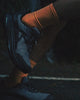 Slow motion stride of person in a blue Roam running shoe with bright orange sock